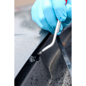 A person wearing blue gloves uses the Sealey Washer Jet Tool - Vauxhall/Opel - AK52207 to tighten a bolt on a wet metal surface.