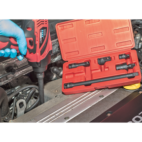 A person wearing a blue glove uses a power drill on a car engine. Next to the engine, an open red case containing the Sealey Premier 6pc Impact Adaptor & Extension Bar Set 1/2"Sq Drive (model AK5514) and various attachments is visible.