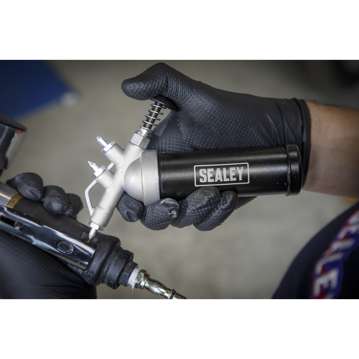 A person wearing black gloves holds and uses the Sealey Mini Grease Gun Push Type - AK55, demonstrating precise placement for optimal efficiency.