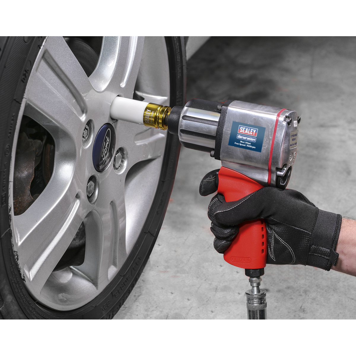 A person wearing a black glove uses a pneumatic impact wrench, fitted with the Sealey Impact Socket & Wheel Nut Removal Set 15pc 1/2"Sq Drive - AK5615M, to tighten a lug nut on a car's wheel.