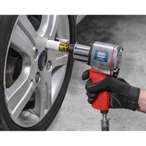A person wearing a black glove uses a pneumatic impact wrench, fitted with the Sealey Impact Socket & Wheel Nut Removal Set 15pc 1/2"Sq Drive - AK5615M, to tighten a lug nut on a car's wheel.
