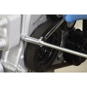 A gloved hand uses a Sealey T-Handle Nut Driver 10 x 300mm - AK5823 to loosen a bolt on an engine component, several pulleys visible in the background.