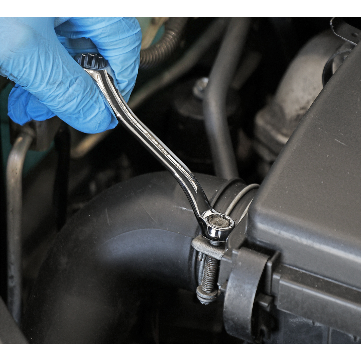 A gloved hand uses a Sealey Double End Ring Spanner Offset Stubby 10 x 13mm (AK63221) to tighten a bolt on a car engine component, showcasing the durability of Chrome Vanadium steel.