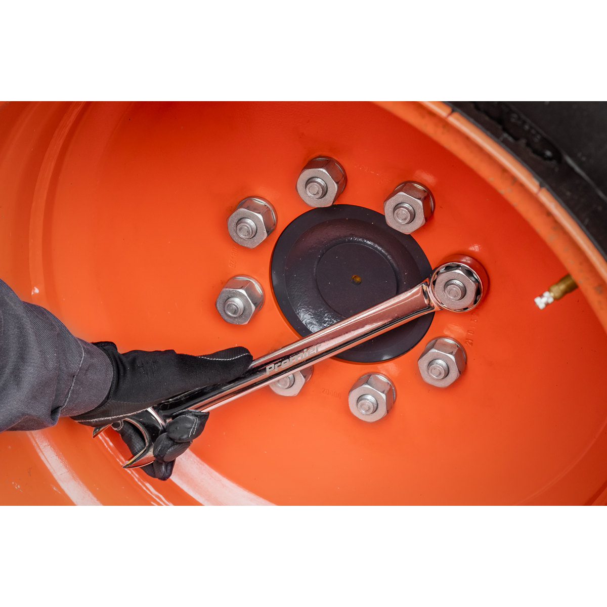 A gloved hand uses a Sealey Combination Spanner Super Jumbo 33mm - AK632433 to tighten a bolt on an orange wheel rim with six visible bolts.