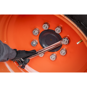 A gloved hand uses a Sealey Combination Spanner Super Jumbo 33mm - AK632433 to tighten a bolt on an orange wheel rim with six visible bolts.