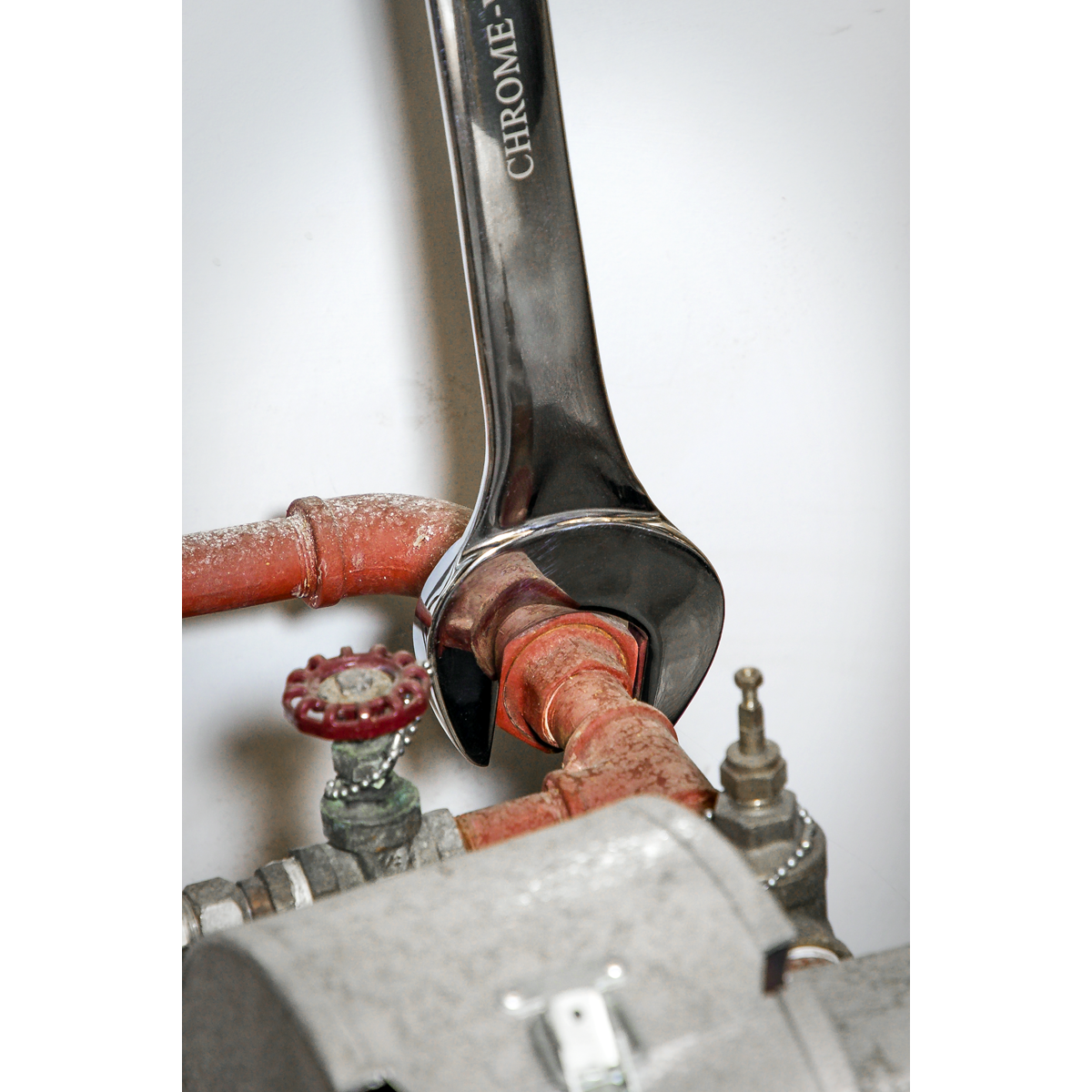 A Sealey Combination Spanner Super Jumbo 42mm - AK632442 tightens a rusted red pipe connection, next to a valve with a red handle and a gray metallic component, illustrating the reliability of Premier Hand Tools for both agricultural and industrial use.