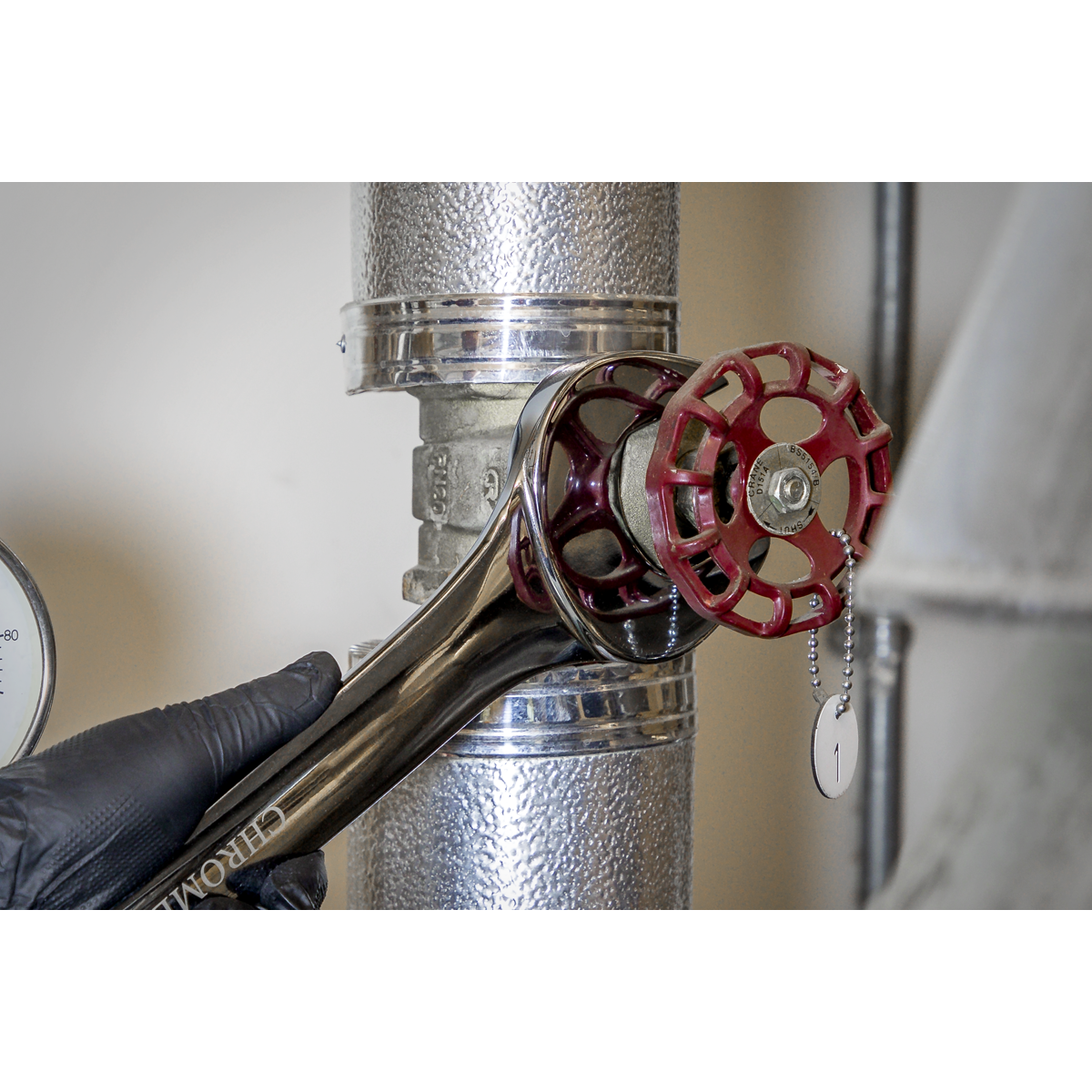 A gloved hand uses a Sealey Combination Spanner Super Jumbo 48mm - AK632448 to adjust a red valve on a metallic pipe, showcasing the tool's corrosion resistance.