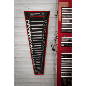 A wall-mounted Sealey Combination Spanner Set 25pc Metric - AK63253, featuring 12-point WallDrive® ring combination spanners, hangs next to a red tool chest in a workshop with white brick walls.
