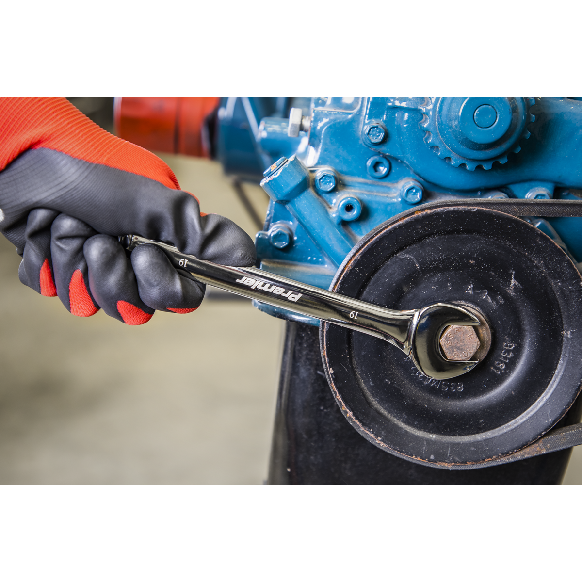 A gloved hand from the Sealey Combination Spanner Set 12pc - Metric - AK63265 uses a wrench to tighten a bolt on a mechanical assembly, showcasing the reliable strength of chrome vanadium steel.