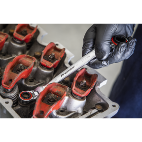 A gloved hand using a Sealey Ratchet Ring Spanner 4-in-1 Flexi-Head Reversible Metric Platinum Series - AK63947 made from Chrome Vanadium steel on a mechanical component with red and rusted parts.