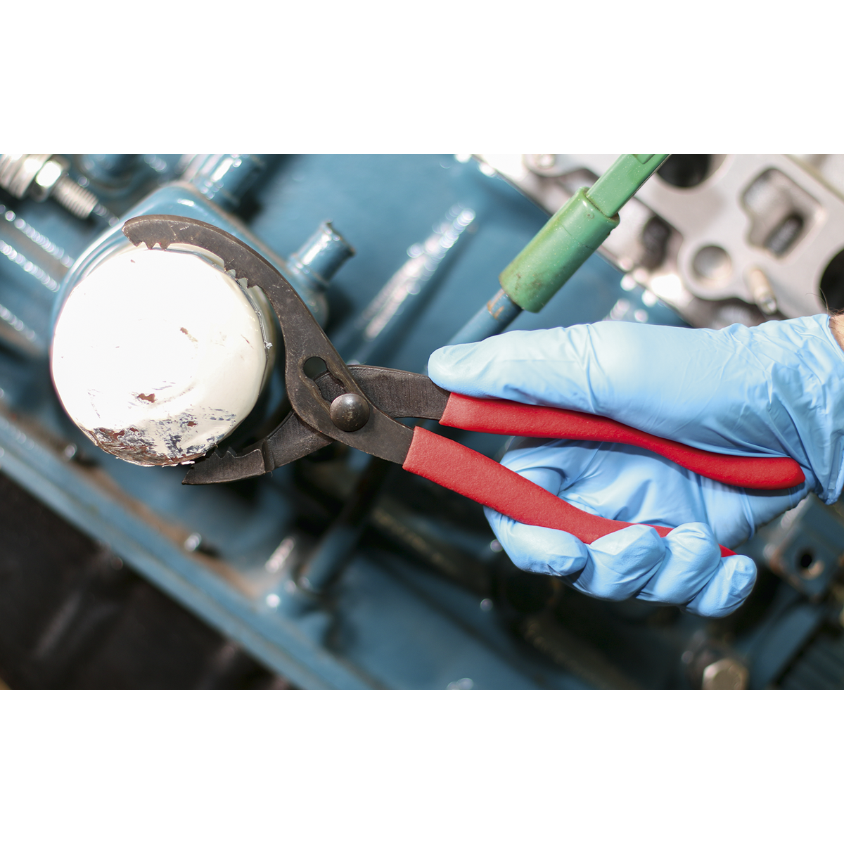 A person wearing blue gloves uses the Sealey Ø60-108mm Capacity Oil Filter Pliers - AK6411 with serrated jaws to remove an oil filter from an engine.