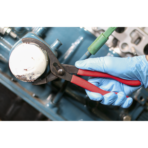 A person wearing blue gloves uses the Sealey Ø60-108mm Capacity Oil Filter Pliers - AK6411 with serrated jaws to remove an oil filter from an engine.
