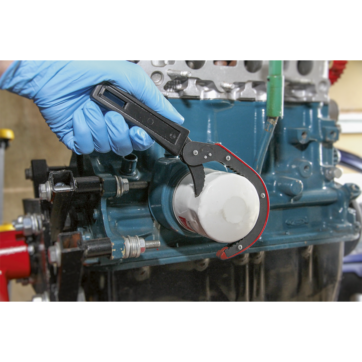 With a firm grip, a gloved hand uses the Sealey Oil Filter Wrench Ø75-95mm - AK6420 to remove an oil filter from a blue engine block.