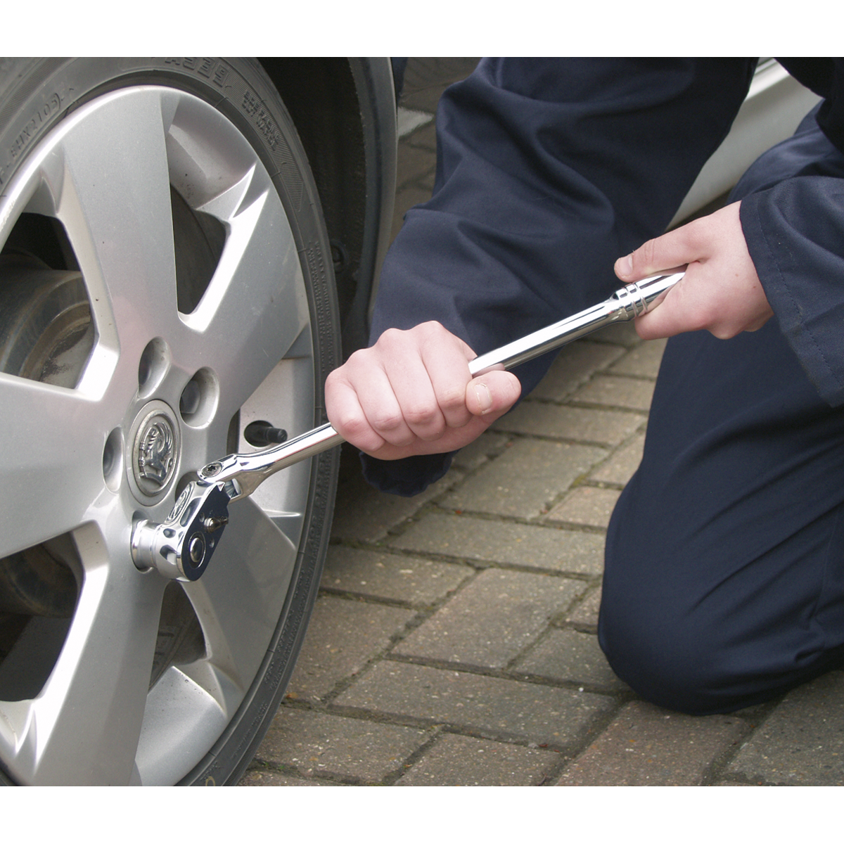 The person is using a Sealey Ratchet Wrench Flexi-Head 445mm 1/2"Sq Drive Pear-Head Flip Reverse - AK662F to tighten a lug nut on a car wheel, confident in the quality backed by a lifetime guarantee.