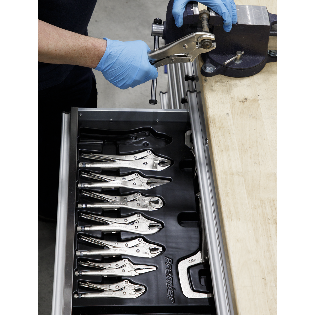 A person wearing blue gloves uses a wrench at a workbench, with an open drawer showcasing organized clamp pliers and Sealey's Locking Pliers Set 10pc - AK6800 for professional use.