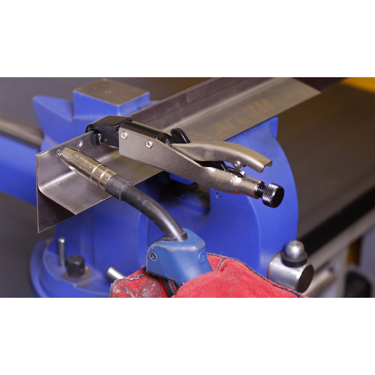 Close-up of the Axial Locking Grip 195mm L-Tip - AK6832 from Sealey holding a metal piece on a blue vise, with a red protective glove visible in the foreground, demonstrating secure clamping and efficient one-handed operation using hand tools.