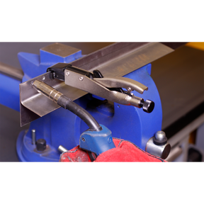 Close-up of the Axial Locking Grip 195mm L-Tip - AK6832 from Sealey holding a metal piece on a blue vise, with a red protective glove visible in the foreground, demonstrating secure clamping and efficient one-handed operation using hand tools.