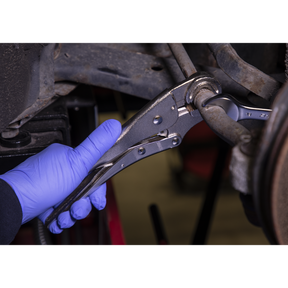 A gloved hand uses Sealey's Locking Pliers Round Jaws 235mm 0-50mm Capacity - AK6872, designed with a reliable locking mechanism, to grip and adjust a metal bolt in an automotive setting.