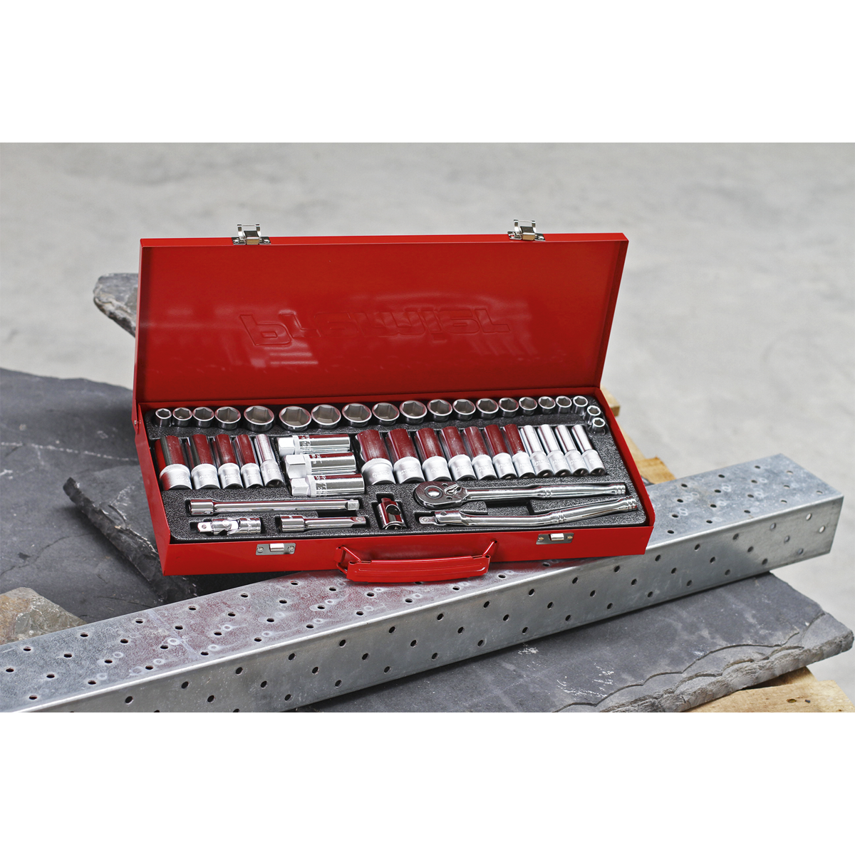 A Sealey Socket Set 45pc 3/8"Sq Drive 6pt WallDrive® - Metric/Imperial (AK692) sits in a red metal toolbox with the lid open, revealing a professional assortment of wrenches and other tools crafted from Chrome Vanadium steel, placed on a piece of metal next to a perforated metal beam. This durable collection guarantees reliability and performance with a lifetime guarantee.