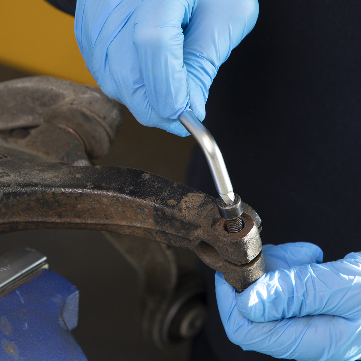 A person wearing blue gloves uses a Sealey Ball-End Hex Key from the 9-piece Extra-Long Lock-On™ Metric Set (AK7180) to tighten or loosen rusted hex head fasteners on a metal part, possibly part of a vehicle or machinery.