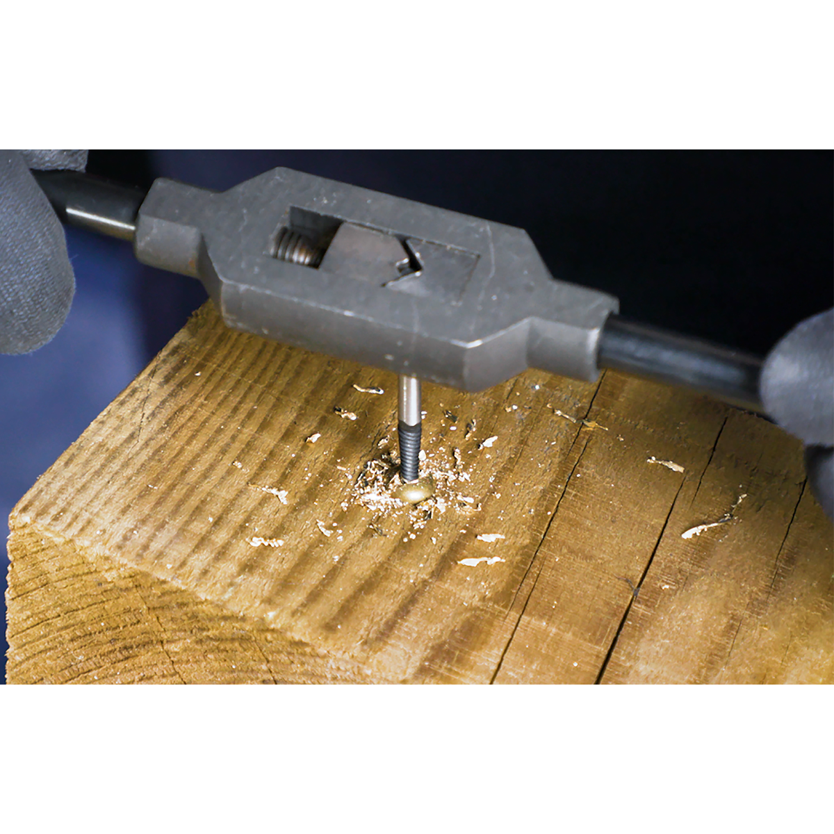 Close-up of a person utilizing a Sealey Screw Extractor Set 5pc Helix Type - AK722, crafted from Chrome Molybdenum steel, to create threads inside a hole in a piece of wood, with sawdust scattered around the work area.