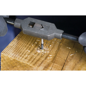 Close-up of a person utilizing a Sealey Screw Extractor Set 5pc Helix Type - AK722, crafted from Chrome Molybdenum steel, to create threads inside a hole in a piece of wood, with sawdust scattered around the work area.