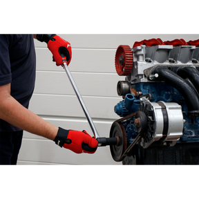 A person wearing red gloves with an anti-slip comfort grip uses a Sealey Breaker Bar 600mm 1/2" Sq Drive - AK7304 on a car engine belt system against a white wall background.