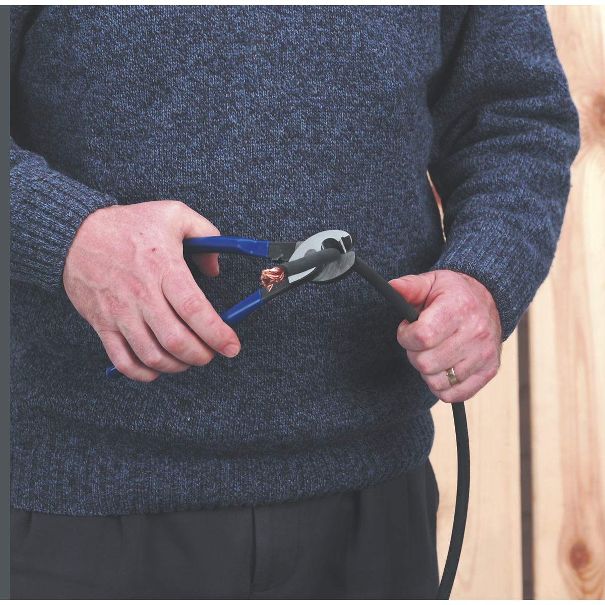 Person wearing a blue sweater uses the Sealey Cable Shears 250mm - AK8358 to cut a thick black cable.