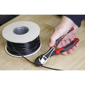 A person using the Sealey Side Cutters High Leverage 190mm Heavy-Duty AK8375, featuring precision ground cutting edges, to cut black electrical wire next to a spool of wire.
