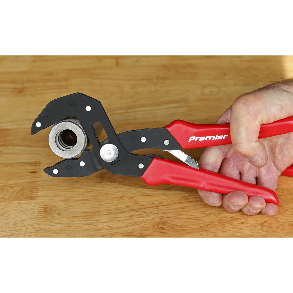 A hand holding Sealey branded multi-grip self-adjusting pliers, model AK8536, with adjustable jaws, gripping a metal bolt against a wooden surface.