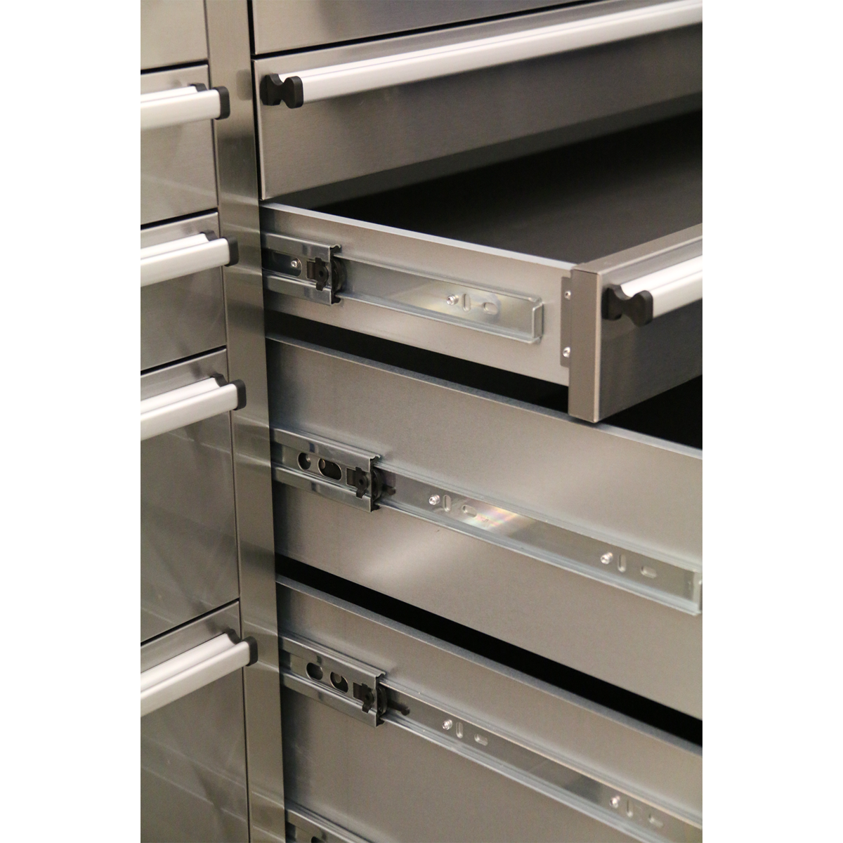 Close-up of metal drawer slides on the Sealey Mobile Stainless Steel Tool Cabinet 10 Drawer & Cupboard - AP7210SS, with several drawers partially open, showcasing the sliding mechanism.