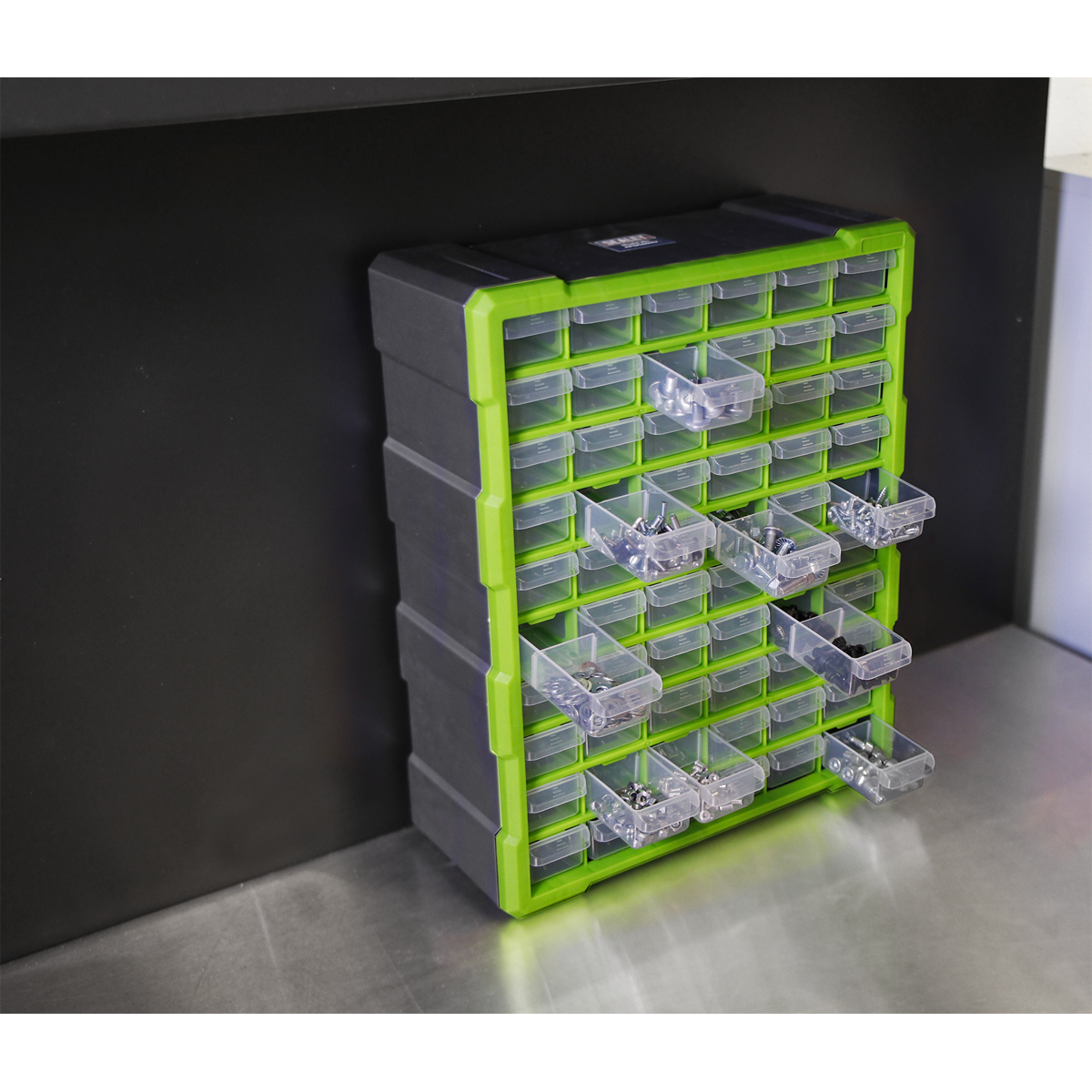 The Sealey Cabinet Box 60 Drawer - Green/Black - APDC60HV, a black and green plastic storage cabinet with impact-resistant, transparent drawers, is perfect for storing fixings and components. It is mounted on a wall above a metallic work surface.