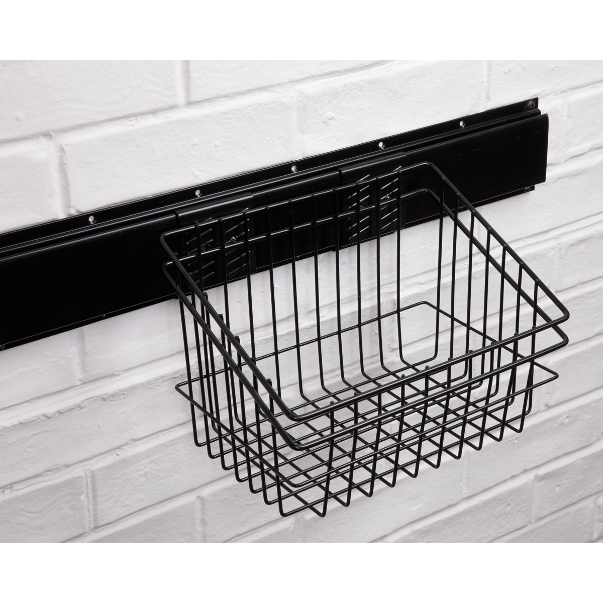 A Sealey Storage Basket - APH14 mounted on a white brick wall using a horizontal black Wall Mountable Storage Rail.