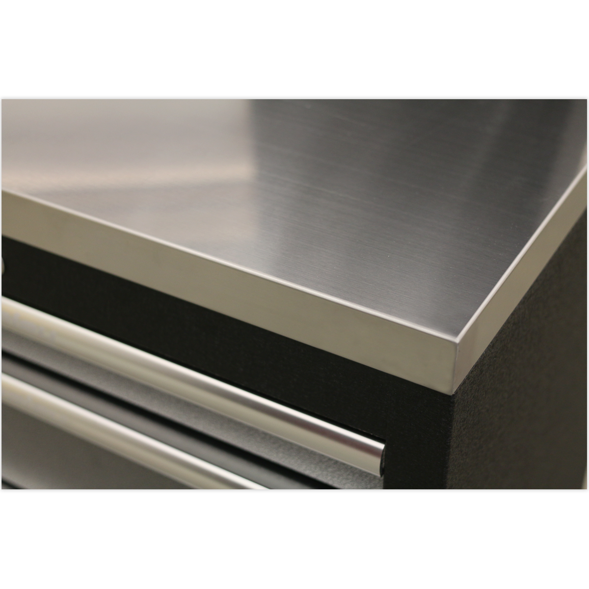 Close-up of a Sealey Stainless Steel Worktop 680mm - APMS50SSA with a corner of a black drawer unit below it. The stainless steel worktop has a brushed finish, and the drawer unit, part of the APMS Floor Cabinets collection, features a horizontal handle.