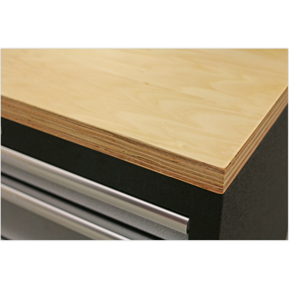 Close-up of a Pressed Wood Worktop 680mm - APMS50WA by Sealey, showcasing its smooth, light-colored surface and layered edges, positioned above a black APMS Floor Cabinet with metal handles. Enjoy peace of mind with the 5 Year Guarantee on every Sealey Pressed Wood Worktop.