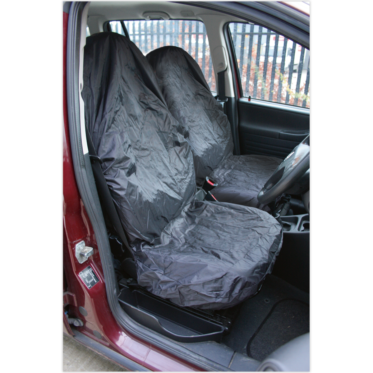 A red vehicle interior featuring Sealey's Front Seat Protector Set 2pc Lightweight - CSC5 on the front seats, made with water-resistant nylon. The opened car door offers a glimpse of the dashboard and steering wheel, emphasizing comprehensive vehicle interior protection.