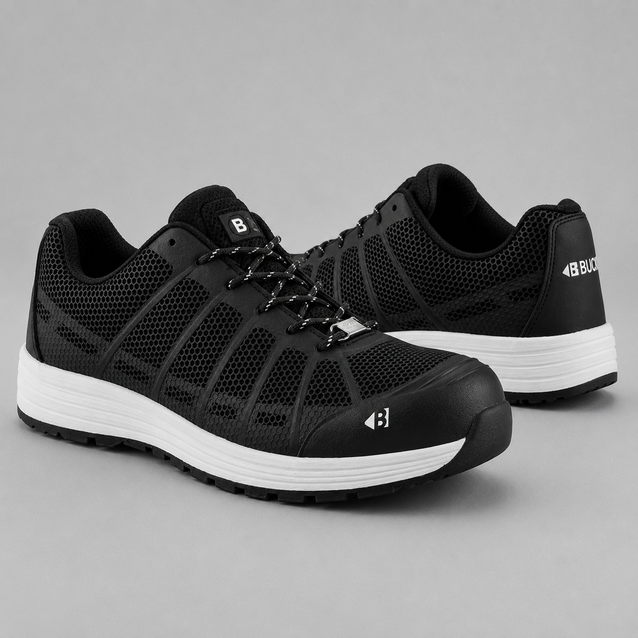 A pair of black protective work shoes with white midsoles, shown from the side and back on a neutral gray background.