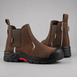 A pair of brown Chelsea-style work boots with black soles and a small red accent on the side, photographed on a neutral gray background.