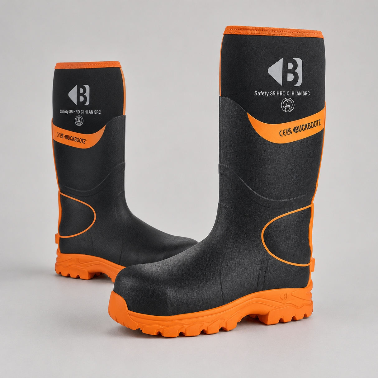 A pair of black and orange safety boots shown on a light gray studio background. The boots feature a black upper with bright orange trim, soles, and accents, along with white branding text and logos.