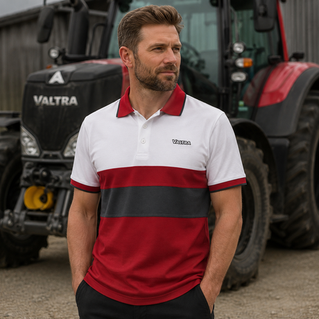 A man wearing a Valtra polo shirt stands in front of a red and black tractor. The polo shirt is white with a red collar and sleeve cuffs, a wide red horizontal stripe, and a black horizontal stripe across the chest.