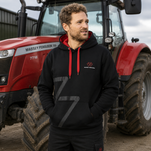 A man wearing a black pullover hoodie with red drawstrings and a red chest logo stands in front of a red Massey Ferguson tractor. The hoodie features a large gray number 7 on the front.