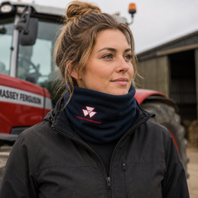 A woman wearing a dark navy Kwantu Agricultural fleece neck warmer with a red logo, standing in front of a red Massey Ferguson tractor on a farm.