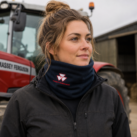 A woman wearing a dark navy Kwantu Agricultural fleece neck warmer with a red logo, standing in front of a red Massey Ferguson tractor on a farm.