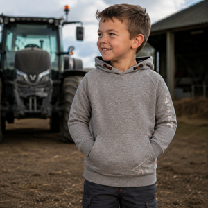A young boy wearing a heather gray pullover hoodie with a kangaroo pocket stands on a farm in front of a tractor and barn.