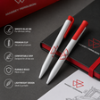 Two Massey Ferguson ballpoint pens with white bodies and red accents are displayed on a dark gray surface next to a black notebook with a red elastic band. The image includes a vertical list of product feature callouts on the left side.