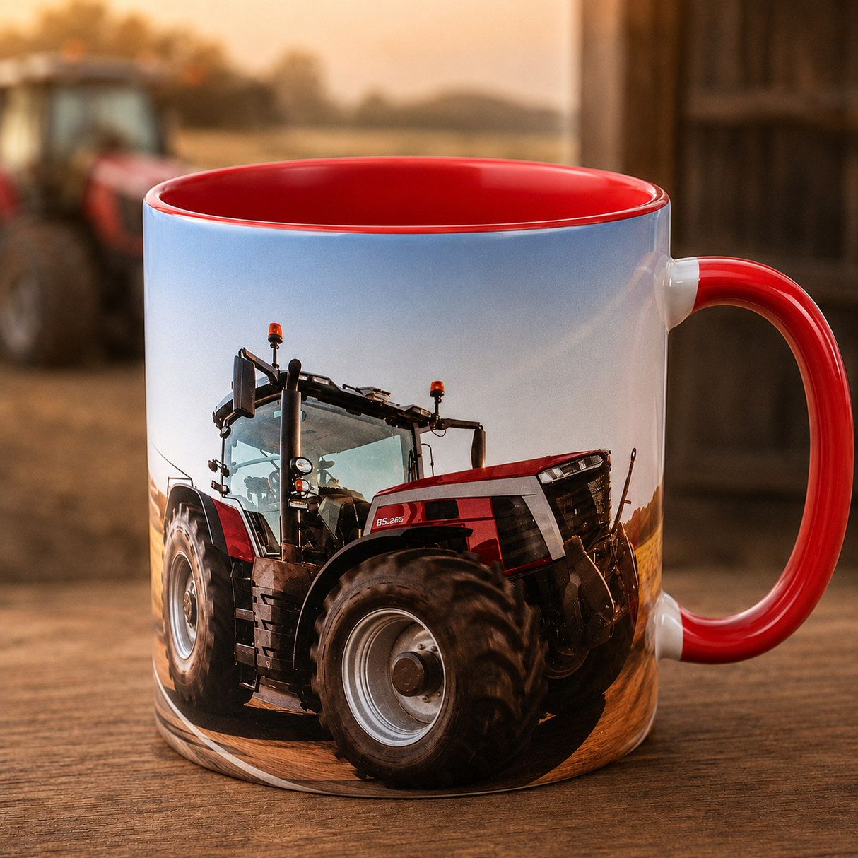 A ceramic mug with a red interior and red handle, printed with a tractor on a farm scene, sitting on a wooden surface with a blurred tractor and barn in the background.