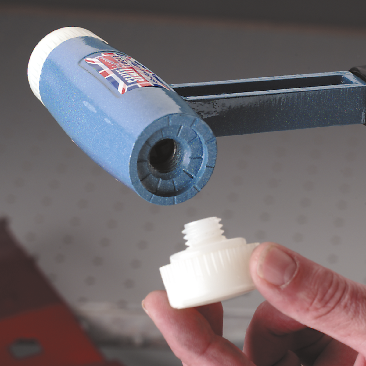 Close-up of a hand holding a white plastic cap near the threaded opening of a blue cylindrical tool with a label, suggesting it's an NFH175 Nylon Hammer Face, Medium/Red for professional use by Sealey.