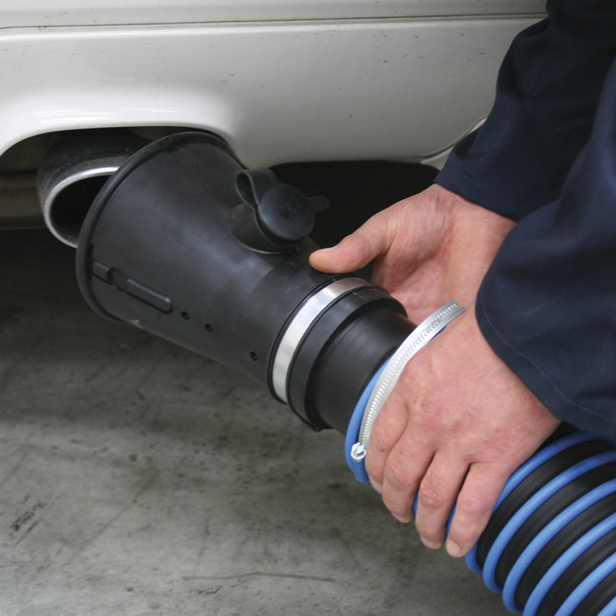 A person attaches a Sealey Exhaust Fume Extractor with 6m Ducting (EFS/93) to the exhaust pipe of a vehicle, using gas analyser probes to ensure accurate readings.