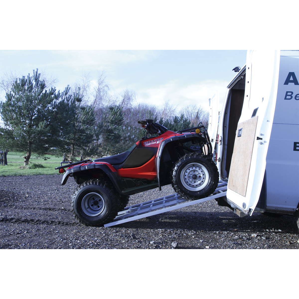 A red ATV is being loaded into a white van using the Sealey Motorcycle/Trike/ATV & Mini Tractor Ramp Wide Tri-Fold 680kg Capacity (FLR680T), set against a background of trees and a gravel surface.