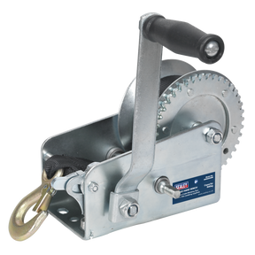 The Sealey Geared Hand Winch 900kg Capacity with Webbing Strap - GWW2000M features a single gear mechanism, a silver finish, a black handle, and a hook attached to a strap. It is mounted on a metal base with hardened steel components and includes a manual brake for added safety.